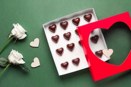 Box with tasty heart-shaped candies and flowers on green backgroundの写真素材