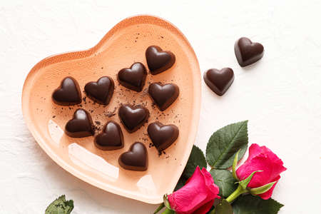 Plate with tasty heart-shaped candies and flowers on white backgroundの写真素材
