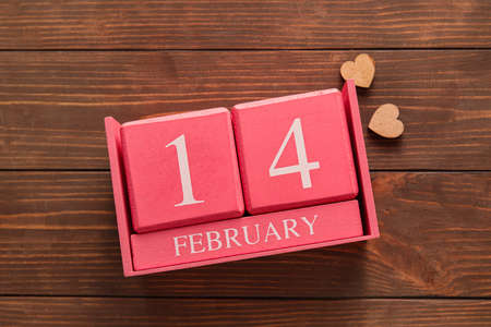 Calendar with date of Valentines Day on wooden background