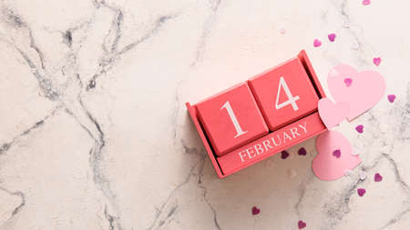 Calendar with date of Valentines Day and heart shaped confetti on white marble background
