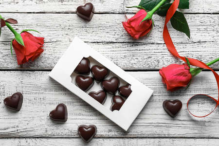 Box with tasty heart-shaped candies and flowers on light wooden backgroundの写真素材