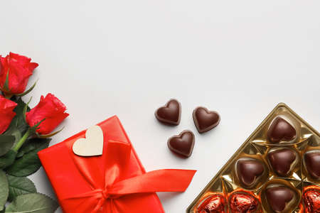 Composition with tasty heart-shaped candies and flowers on white background
