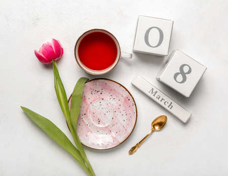 Calendar, cup of tea and flower for International Women's Day celebration on light background