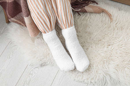Woman in soft warm socks sitting in chair at home. Concept of heating season