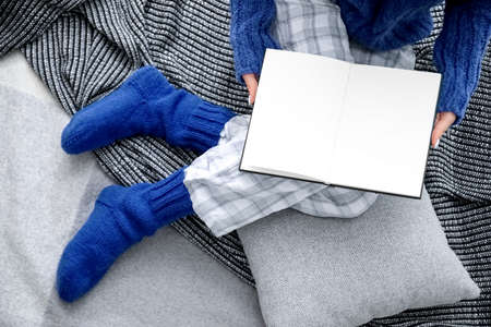 Woman in warm knitted socks sitting on plaid with opened book. Concept of heating seasonの写真素材