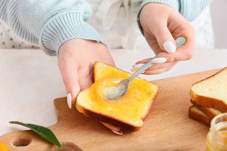 Woman spreading tasty orange jam onto toast at table in kitchen, closeupの写真素材