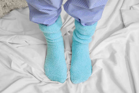 Woman in warm knitted socks on bed, closeup. Concept of heating seasonの写真素材