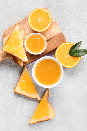 Bowls of tasty orange jam and toasts on light background