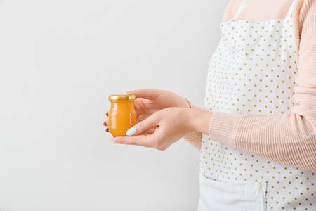 Woman holding jar of tasty orange jam on light backgroundの写真素材