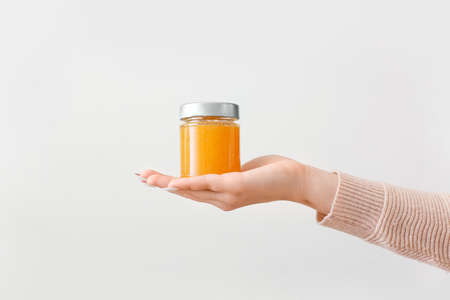 Female hand with jar of tasty orange jam on light backgroundの写真素材