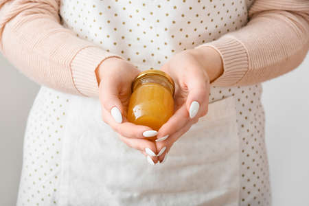 Woman holding jar of tasty orange jam on light backgroundの写真素材