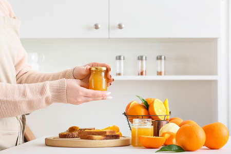 Woman with jar of tasty orange jam in kitchen