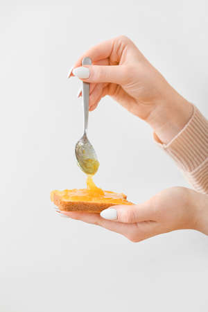 Woman spreading tasty orange jam onto toast on light backgroundの写真素材
