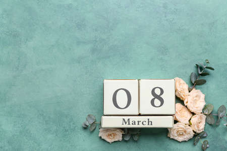 Calendar with date of International Women's Day and flowers on green background