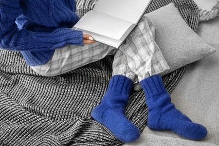 Woman in warm knitted socks sitting on plaid with book. Concept of heating season
