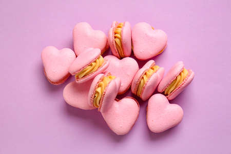 Tasty heart-shaped macaroons on purple background