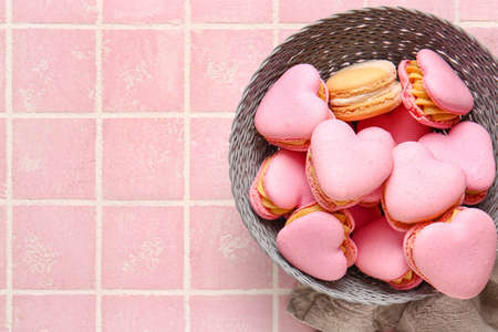 Bowl with tasty heart-shaped macaroons on pink background