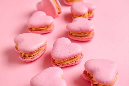 Tasty heart-shaped macaroons on pink background, closeup