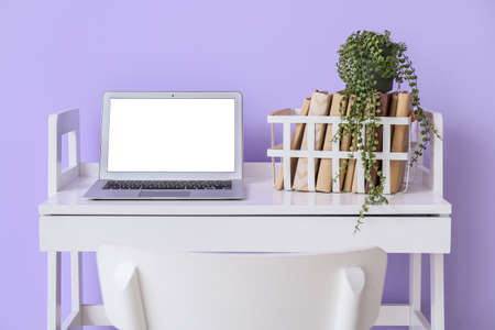 Modern workplace with laptop, books and houseplant near violet wallの写真素材