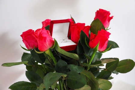 Box with engagement ring and bouquet of roses near light wall