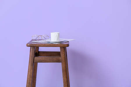 Wooden bar stool with cup of coffee, eyeglasses and newspaper near violet wallの写真素材