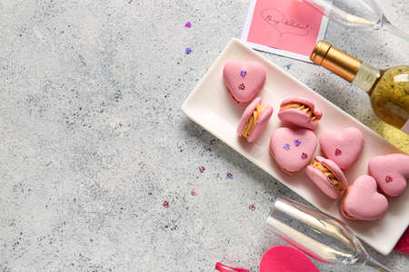 Plate with tasty heart-shaped macaroons and glass on light backgroundの写真素材