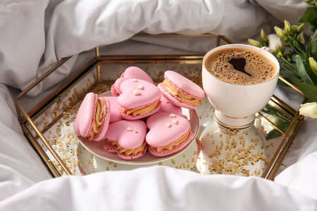 Tray with tasty heart-shaped macaroons and cup of coffee on bedの写真素材