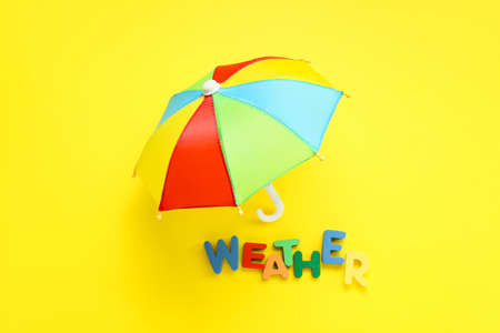 Mini umbrella and word WEATHER made of colorful letters on yellow backgroundの写真素材