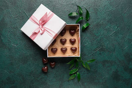 Box with tasty heart-shaped candies and plant leaves on dark color background