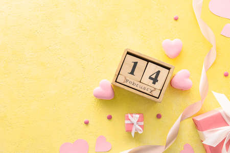 Calendar with date of Valentines Day, gift boxes and tasty macaroons in heart shape on yellow backgroundの写真素材