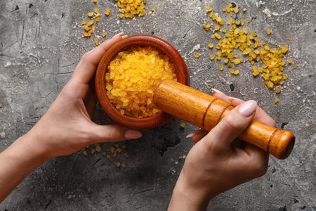 Woman holding wooden mortar with orange sea salt on grunge background, closeup