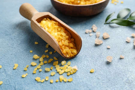 Wooden scoop of orange sea salt on color background, closeup