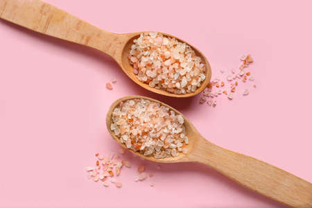 Wooden spoons with sea salt on pink background, closeup