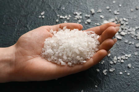 Female hand with sea salt on dark color background, closeup