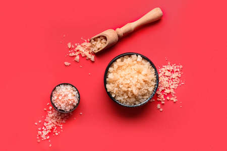 Bowls and scoop of sea salt on red background