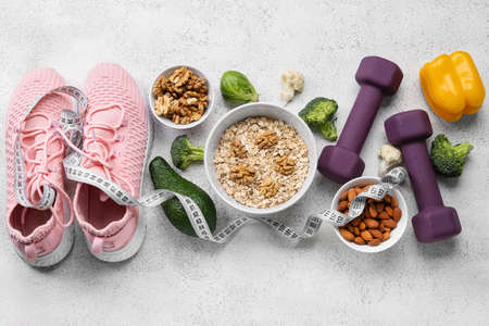 Bowls with healthy food, sneakers, dumbbells and measuring tape on light background. Diet conceptの写真素材