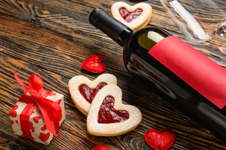 Tasty cookies in heart shape and bottle of wine on wooden backgroundの写真素材