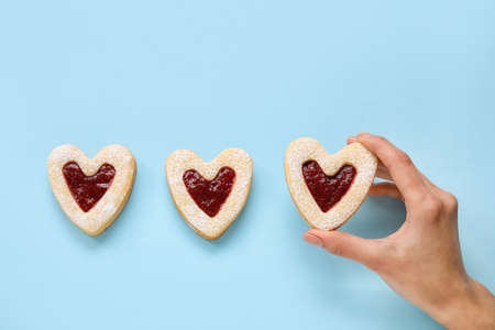 Female hand with tasty cookies in heart shape on blue backgroundの写真素材