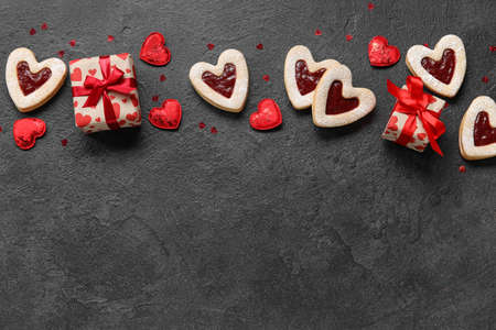 Tasty cookies in heart shape and gift boxes on dark background
