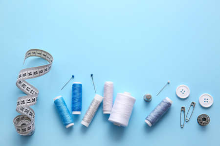 Thread spools, measuring tape, buttons and pins on blue background