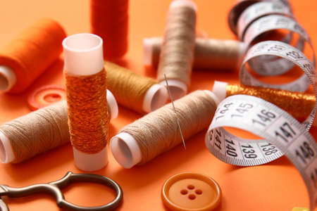 Thread spools with measuring tape and buttons on orange background, closeupの写真素材