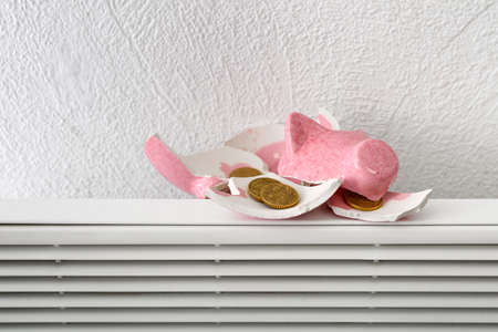 Broken piggy bank with coins on radiator near white wall. Concept of heating seasonの写真素材