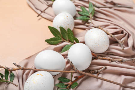Beautiful Easter eggs, tree branches, leaves and cloth on color background, closeupの写真素材