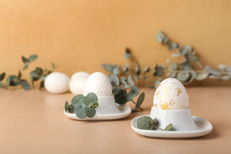 Holders with beautiful Easter eggs and eucalyptus branches on color background
