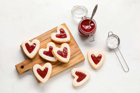 Board with tasty cookies and jam for Valentine's Day celebration on light background