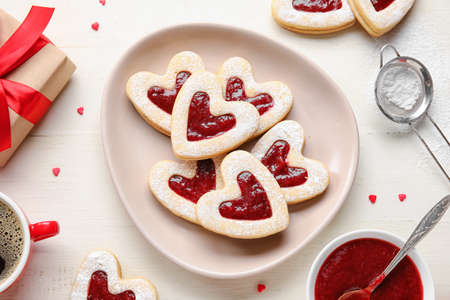 Plate with tasty cookies and cup of coffee for Valentine's Day celebration on light background