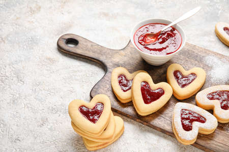 Board with tasty cookies and jam for Valentine's Day celebration on light background, closeup
