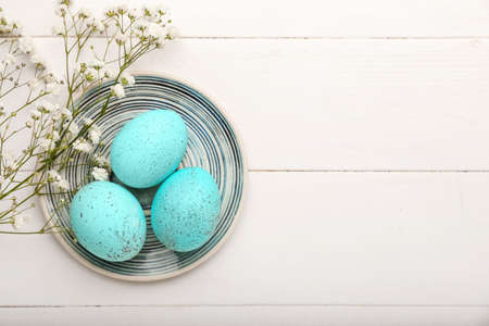 Plate with beautiful Easter eggs and gypsophila flowers on light wooden background