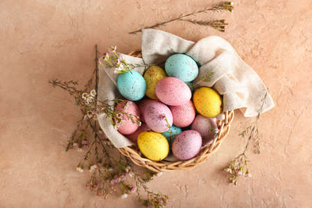 Basket with beautiful Easter eggs and flowers on color background
