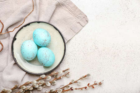 Composition with plate of beautiful Easter eggs and pussy willow branches on light backgroundの写真素材